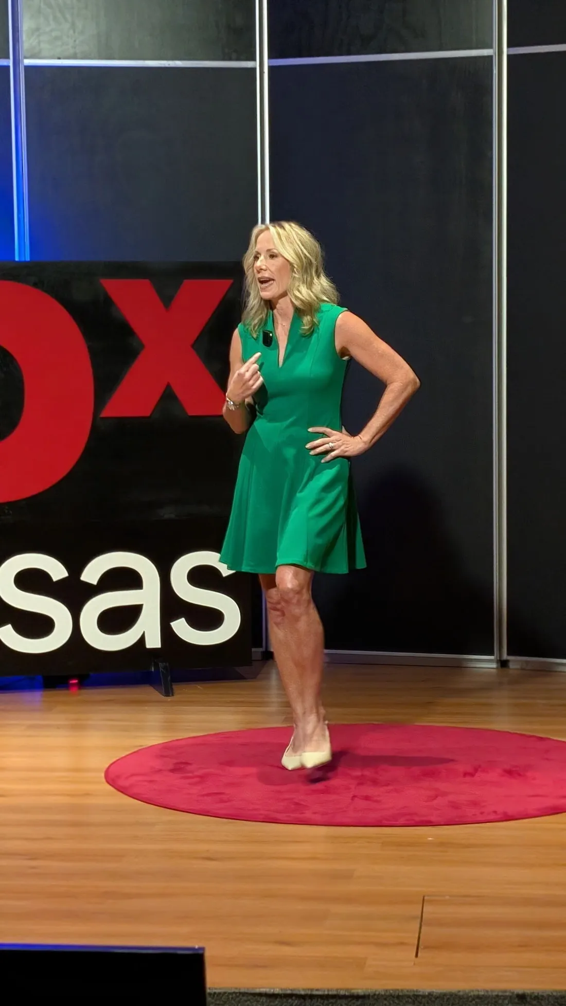 Carolyn Johnson speaking on the TEDx stage in a green dress